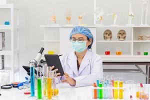une femme scientifique asiatique recherche une formule chimique dans un laboratoire dans une tablette à main.