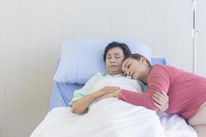 une femme asiatique embrasse sa mère qui récupère sur un lit d'hôpital. photo