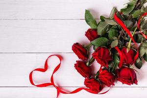 ruban rouge en forme de coeur, bouquet de roses et coffrets cadeaux enveloppés dans du papier kraft sur une table en bois blanche. photo