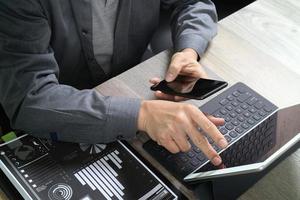 vue de dessus de la main d'un homme d'affaires utilisant un smartphone, des achats en ligne de paiements mobiles, un canal omni, un clavier d'accueil pour tablette numérique, des documents, dans un bureau moderne sur un bureau en bois photo