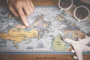 la main des voyageurs planifie un voyage de vacances sur la carte du monde photo