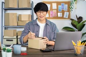 homme asiatique entrepreneur démarrage petite entreprise entrepreneur PME homme indépendant travaillant avec la boîte à l'emballage de marketing en ligne et scène de livraison au bureau à domicile, concept de vendeur en ligne. photo