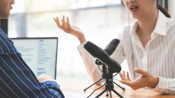 animatrices de radio asiatiques faisant des gestes vers le microphone tout en interviewant un homme invité dans un studio tout en enregistrant un podcast pour une émission en ligne en studio ensemble