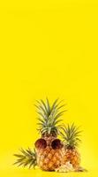 ananas créatif levant les yeux avec des lunettes de soleil et une coquille isolée sur fond jaune, modèle de conception d'idée de plage de vacances d'été, espace de copie en gros plan photo