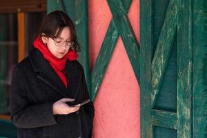 une fille avec un téléphone dans les mains se tient dans la rue près d'une maison rose aux volets verts photo