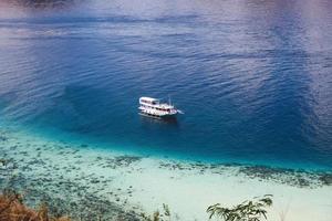 bateau en bois phinisi blanc naviguant sur une belle mer avec de l'eau bleue transparente photo