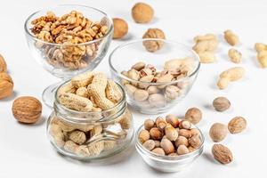 cacahuètes, noix, pistaches et noisettes dans des bols en verre et dans un bocal sur fond blanc photo