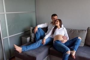 un homme et une femme enceinte sont assis enlacés sur le canapé. photo