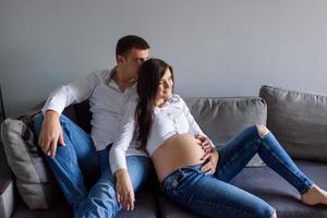 un homme et une femme enceinte sont assis enlacés sur le canapé. photo