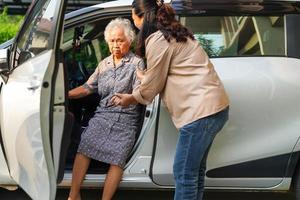 le soignant aide une patiente asiatique âgée handicapée à monter dans sa voiture, concept médical. photo