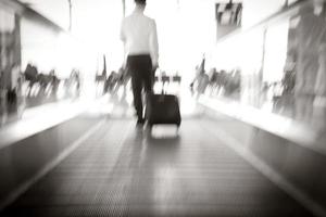 flou, homme d'affaires traînant une petite valise à bagages dans le couloir de l'aéroport marchant jusqu'aux portes d'embarquement photo