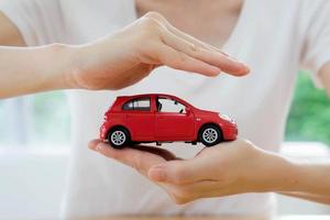 mains d'une femme d'affaires tenant une petite voiture rouge isolée photo