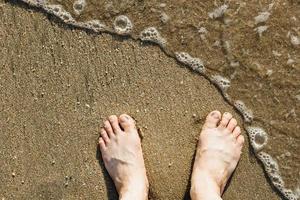 Pieds masculins caucasiens asiatiques sur le sable avec une vague entre, en vacances.copie espace.vue de dessus photo