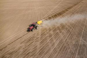 vue aérienne d'un tracteur avec semoir monté effectuant un semis direct de cultures sur un champ agricole labouré. l'agriculteur utilise des machines agricoles pour le processus de plantation, vue de dessus photo