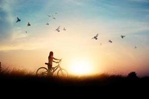 femme solitaire debout avec un vélo sur la route de la rizière parmi les oiseaux volants et fond de coucher de soleil photo