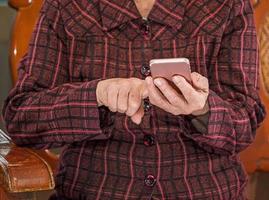 femme âgée asiatique assise et regardant à travers quelque chose sur un smartphone moderne, établissant une connexion avec d'autres à la maison, technologie vivante, gros plan photo