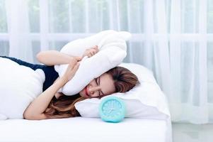 la femme a enlevé l'oreiller de l'oreille pendant que le réveil sonnait le matin. l'idée de se lever pour aller travailler à l'heure photo