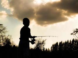 silhouette d'un enfant pêchant le temps heureux des enfants au milieu de la nature au coucher du soleil photo