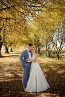 jeune beau couple étreignant dans leurs robes de mariée dans le parc d'automne. photo