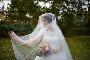 portrait d'une mariée solitaire sur fond de parc d'automne. la jeune fille s'est réfugiée sous un voile avec lequel le vent se développe. photo