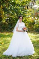 portrait d'une mariée solitaire sur fond de parc d'automne. la jeune fille s'est réfugiée sous un voile avec lequel le vent se développe. photo