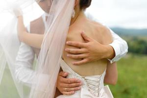 la mariée et le marié s'étreignent sous un voile et s'inclinent doucement la tête l'un vers l'autre. photo