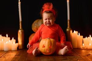 petite fille est assise sur un fond de citrouilles jack et de bougies sur fond noir. photo