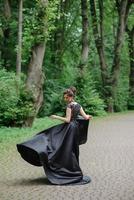 belle jeune femme posant dans une robe noire dans un parc. photo