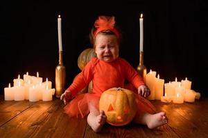 petite fille est assise sur un fond de citrouilles jack et de bougies sur fond noir. photo