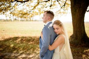 jeune beau couple étreignant dans leurs robes de mariée dans le parc d'automne. photo