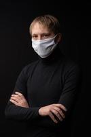 un homme portant un masque médical regarde la caméra. tourné sur un fond noir. photo