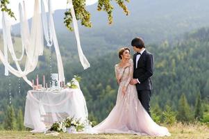 la mariée et le marié s'embrassent sous un vieux chêne. séance photo de mariage à la montagne. à côté d'eux se trouve un décor préparé pour la cérémonie.