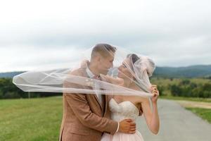 la mariée et le marié s'étreignent sous un voile et s'inclinent doucement la tête l'un vers l'autre. photo