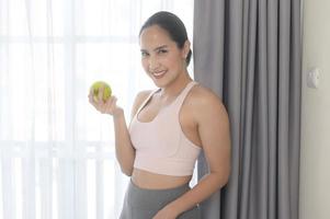 jeune femme en forme mangeant une pomme après l'entraînement à la maison, concept de sport et de mode de vie sain. photo