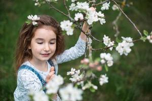 une jolie petite fille de 5 ans dans un verger de pommiers blancs en fleurs au printemps. printemps, verger, floraison, allergie, parfum printanier, tendresse, soin de la nature. portrait photo