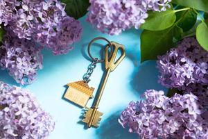 clé de la maison avec porte-clés sur fond de printemps bleu et branches lilas.maison de vacances d'été, réservation d'un chalet à la campagne, déménagement dans une nouvelle maison, hypothèque, location et achat immobilier. tourisme photo