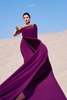 incroyable belle femme brune avec la plume de paon en tissu violet dans le désert. oriental, indien, mode, concept de style photo