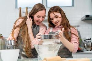 la mère et la fille aiment faire de la boulangerie ensemble dans la cuisine. petite fille tamisant la farine se prépare à faire de la pâte. bonne activité familiale le week-end. enfant apprenant à cuisiner. photo