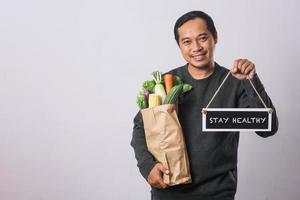 homme tenant un sac d'épicerie avec des légumes et une planche qui dit rester en bonne santé photo