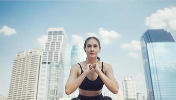 femme sportive accroupie pour s'échauffer avant l'entraînement physique. femme athlète faisant des exercices d'étirement dans la rue de la ville près de bâtiments à plusieurs étages. photo