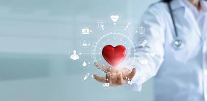 docteur en médecine tenant une forme de coeur rouge à la main avec une connexion réseau d'icônes médicales interface d'écran virtuel moderne, esprit de service et concept de réseau de technologie médicale photo