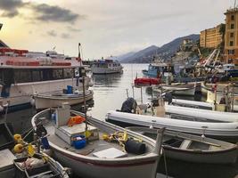 vue sur le port de pêche de camogli, au coucher du soleil, région ligure, nord de l'italie. au mouillage, plusieurs bateaux de pêche et bateaux de tourisme. photo