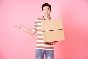 image d'un jeune homme asiatique tenant du carton sur fond rose photo