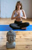 jeune femme en forme de vêtements de sport assis en position du lotus avec la tête de bouddha à l'intérieur. concept de yoga, de détente et de sport photo