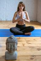 jeune femme en forme de vêtements de sport assis en position du lotus avec la tête de bouddha à l'intérieur. concept de yoga, de détente et de sport photo