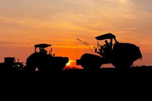 silhouette de machines de construction sur fond de coucher de soleil sur le chantier de construction de routes, tracteur à roues lourdes, niveleuse, compacteurs et autres