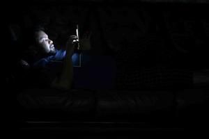 jeune homme assis sur le lit à l'aide d'un téléphone intelligent la nuit photo