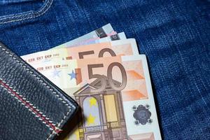 argent en euros, billet en euros à l'intérieur d'un portefeuille en cuir noir sur fond de jean. photo