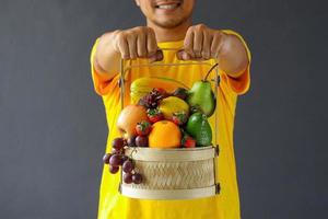 gros plan d'un assortiment de fruits dans un panier tenant par un homme souriant photo