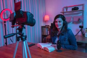 belle femme hispanique devant une caméra vidéo enregistrant un blog dans son studio avec des lumières rouges et bleues à l'intérieur de sa maison
